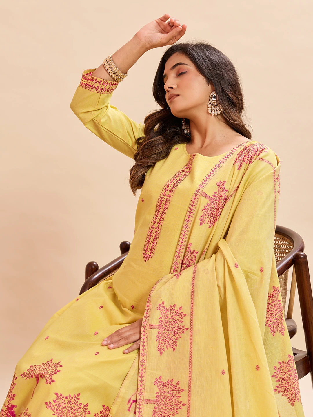 Woman wearing a yellow embroidered traditional outfit with a beige background